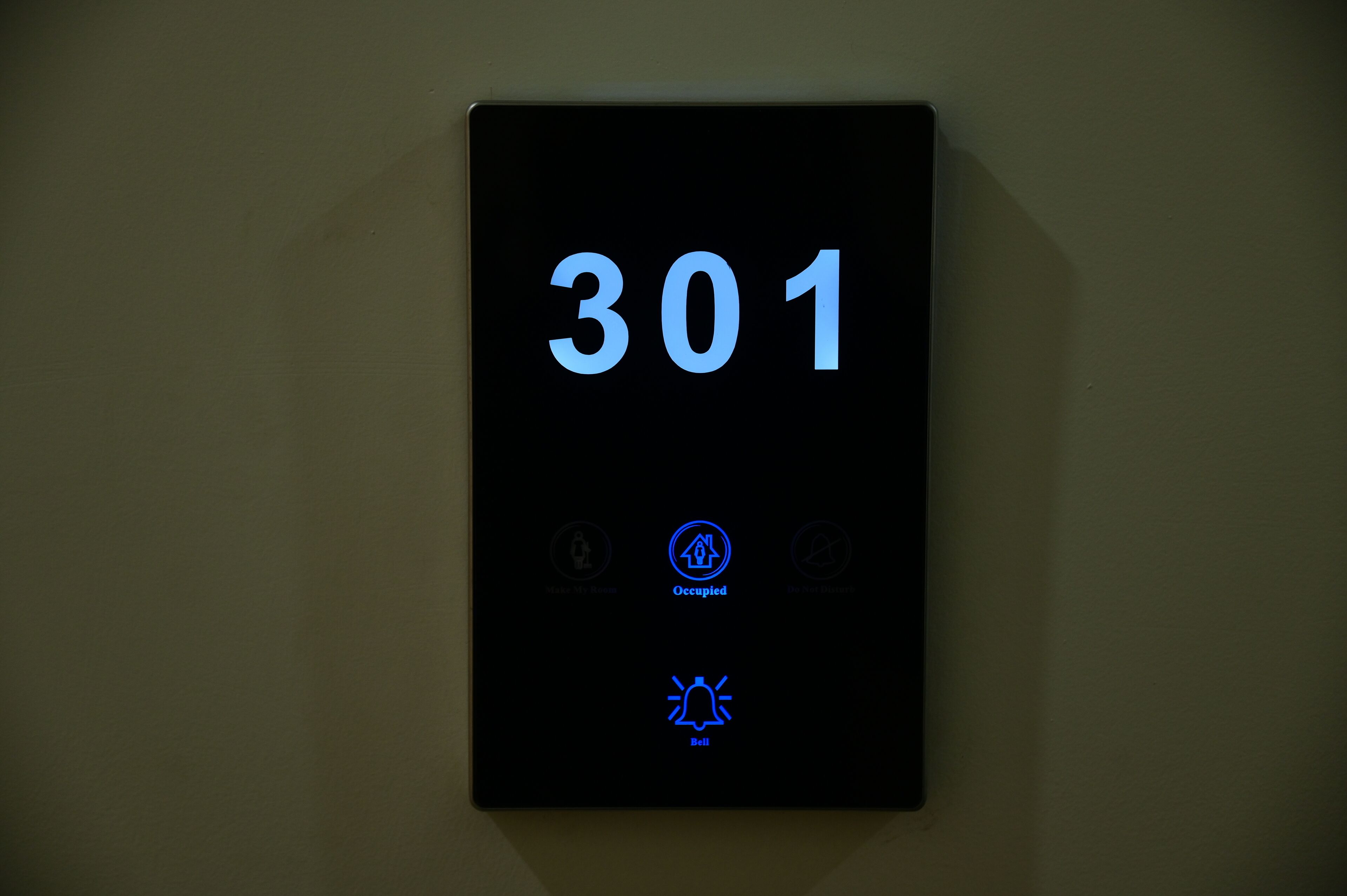 Pantalla digital que muestra el número 301 e iconos que indican servicios de la habitación, como ocupación, teléfono y timbre.