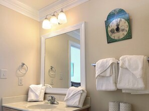 Une salle de bain avec un grand miroir, deux lavabos, un porte-serviettes avec des serviettes et une horloge murale.