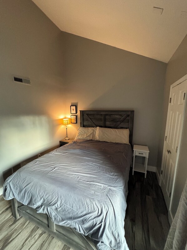 A bedroom with a bed, bedside tables, a nightstand, a wall-mounted lamp, and a door. - Completely Updated Condo-Resort Living on Lake Monroe w/ Pool, Golf + Golf Cart (Bloomington)