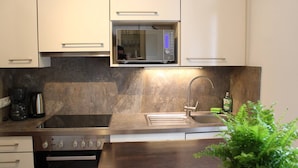 A modern kitchen with white cabinets, a stainless steel sink, a microwave, a stove, and a coffee maker.