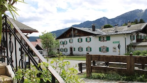 A traditional building with a white facade and green shutters, set against a mountainous backdrop.