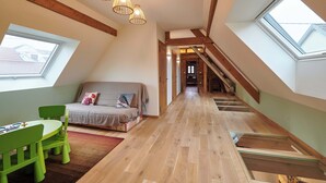 Dormitorio tipo loft con tragaluces, vigas de madera, un sofá verde, una mesa verde y una escalera.