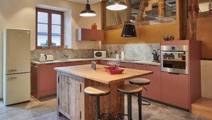 Una cocina con una isla de madera, taburetes de bar, un refrigerador, un microondas y un horno.