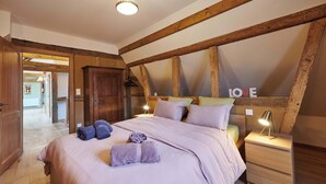 Un dormitorio con techo de madera, una cama con almohadas y una manta, una mesita de noche con lámpara y un armario de madera.