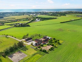 Una propiedad rural con un amplio campo verde, una casa roja y vistas al mar.