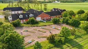A large, red building with multiple sections, surrounded by green fields and trees. - 5 Star Holiday Home in Hjorring (Hjørring)