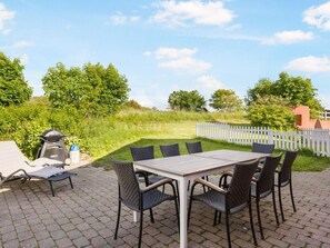 An outdoor patio with a table and chairs, a grill, and a white picket fence. - 5 Star Holiday Home in Hjorring (Hjørring)