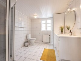 Un baño moderno con inodoro, ducha, lavabo con espejo y ventana.