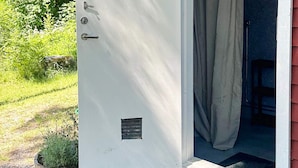 A white door with a small vent and a handle, leading to a room with a red exterior and a window with a curtain. - 2 Person Holiday Park Home in Vaxholm (Vaxholm)