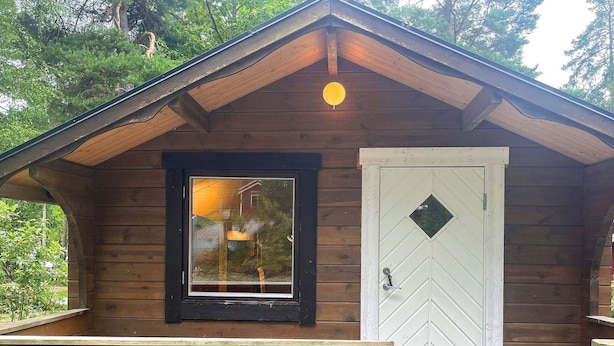 A wooden cabin with a large window and a white door with a diamond-shaped window. - 2 Person Holiday Park Home in Vaxholm (Vaxholm)