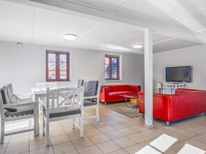 A modern living room with a red sofa, white chairs, a TV, and windows with blinds. - 5 Star Holiday Home in Blokhus (Blokhus)