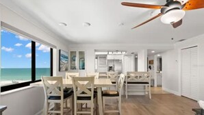 A spacious dining area with a view of the ocean, wooden flooring, and a ceiling fan.