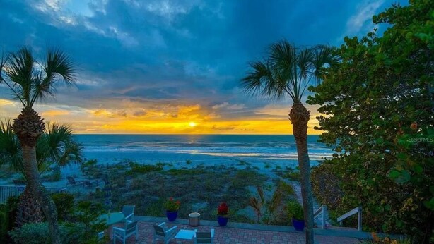 A patio with outdoor seating overlooking a beach at sunset.