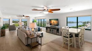 A spacious living room with a large TV, dining area, and a view of the water.