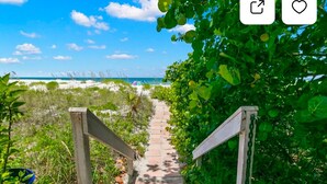 A pathway leading to a beach with a wooden railing on one side and dense greenery on the other.
