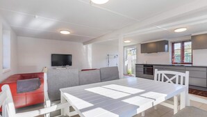 A modern living space with a white dining table, red sofa, grey sectional, and a kitchen area with a TV and window. - 5 Star Holiday Home in Blokhus (Blokhus)