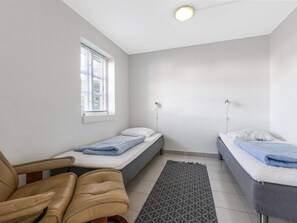 A small, single-room accommodation with a bed, a chair, a window, and a ceiling light. - 5 Star Holiday Home in Blokhus (Blokhus)