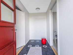 Un couloir avec une porte rouge, un tabouret rouge et un revêtement de sol à motifs.