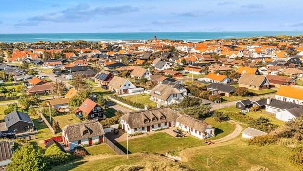 An aerial view of a coastal town with houses, a thatched-roof building, and a beach in the background. - 5 Star Holiday Home in Blokhus (Blokhus)