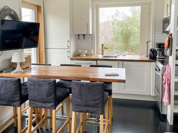 Cozinha moderna com mesa e cadeiras de madeira, forno embutido e janela com vista para o exterior.