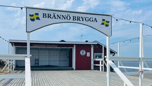 A wooden pier leading to a red building with a Swedish flag, labeled "BRÄNNÖ BRYGGA". - 4 Star Holiday Home in Branno (Branno)