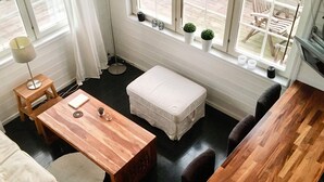 A compact living space with a wooden dining table, a small white sofa, a round coffee table, and a white ottoman. There are two windows with potted plants on the windowsill. - 4 Star Holiday Home in Branno (Branno)