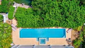 Luchtbeeld van een resort met een rechthoekig zwembad, omringd door weelderige begroeiing en een zandstrand.