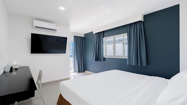 Una habitación de hotel moderna con una cama grande, un televisor de pantalla plana montado en la pared, un escritorio con una silla y una ventana con cortinas.