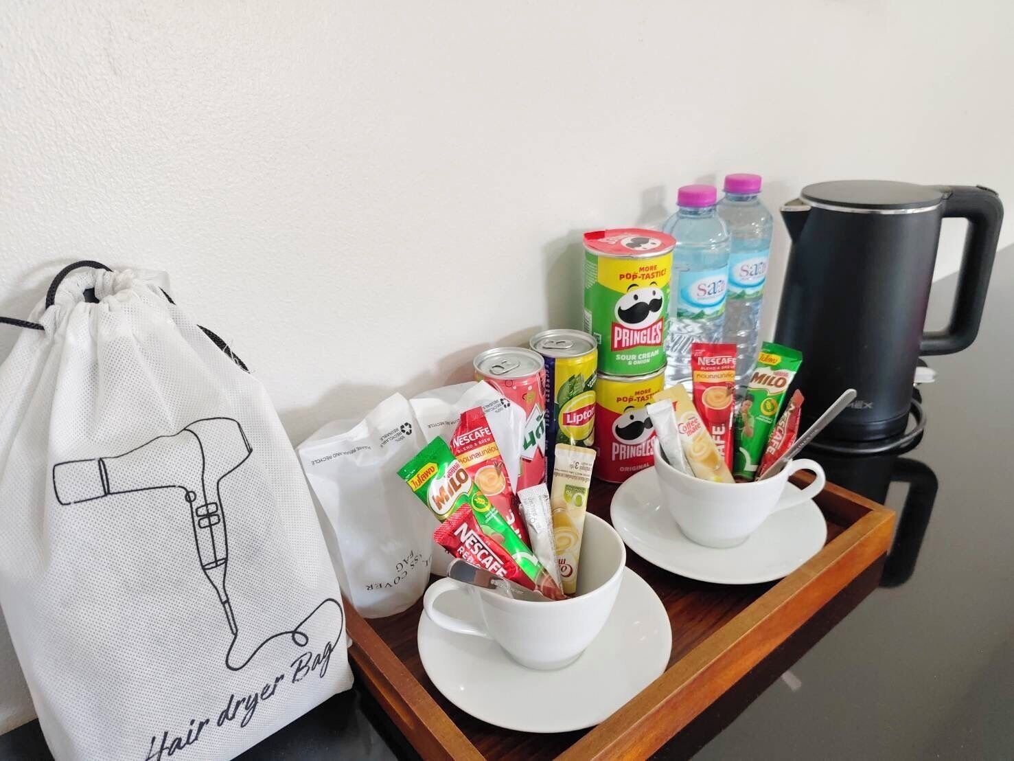 A tray with a coffee maker, cups, and various food items including Pringles and Lipton tea.