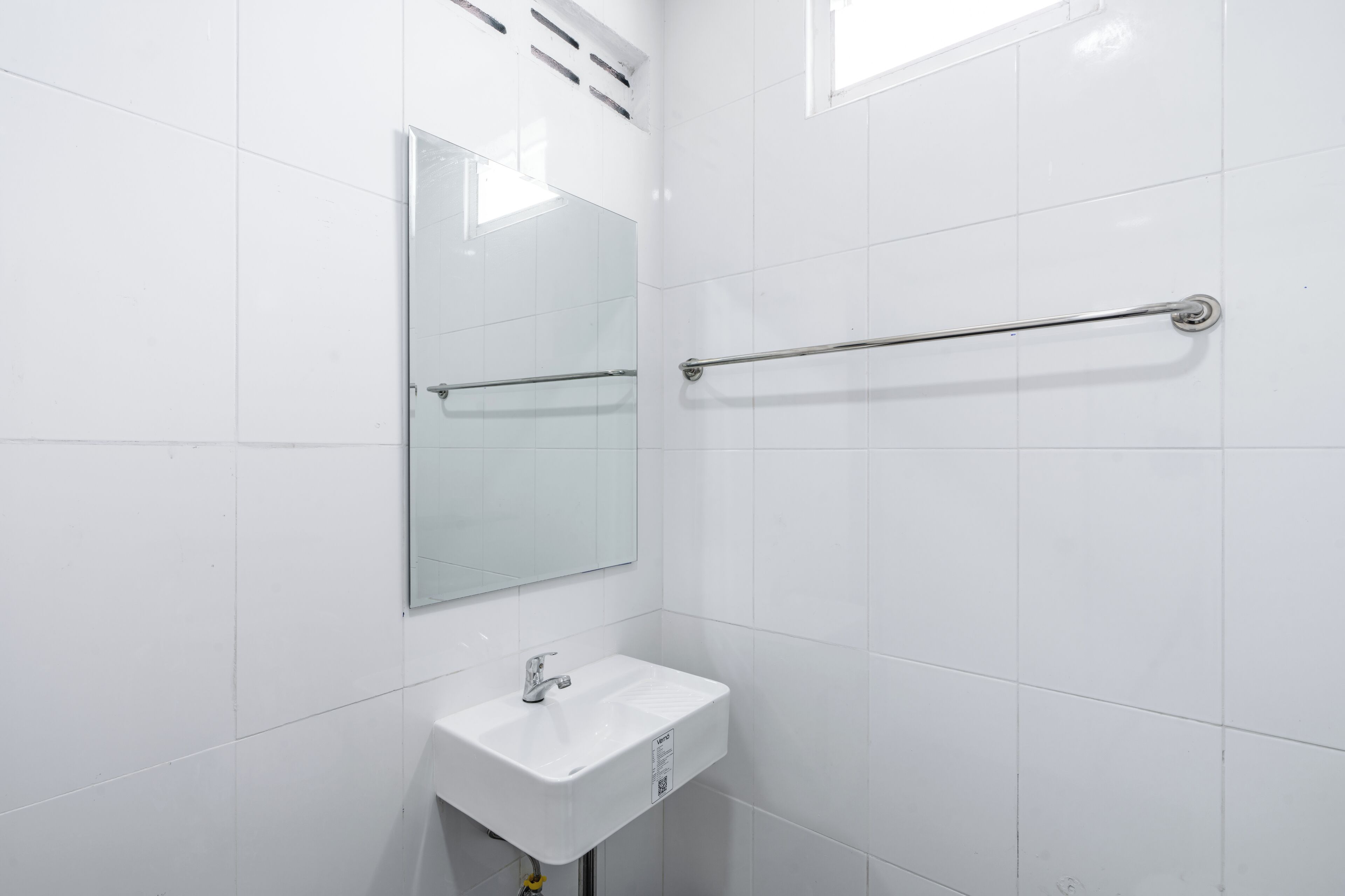 A bathroom with white tiled walls, a sink, a mirror, and a handrail.