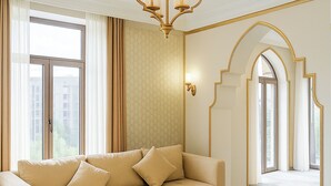 A spacious living room with a beige sofa, a round coffee table, and a chandelier. - Siab Hotel (Samarkand)