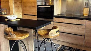 A modern kitchen with wooden cabinetry, a black countertop, and two wooden stools. - Cosy chalet at the foot of the bossons glacier opposite the ski shuttles (Chamonix-Mont-Blanc)
