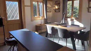 A kitchen with a wooden table and chairs, a window with curtains, and a cabinet. - Cosy chalet at the foot of the bossons glacier opposite the ski shuttles (Chamonix-Mont-Blanc)