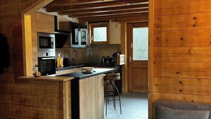 A compact kitchen with wooden cabinetry, a central island, and a bar stool. - Cosy chalet at the foot of the bossons glacier opposite the ski shuttles (Chamonix-Mont-Blanc)