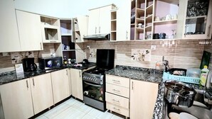 A compact kitchen with a stove, microwave, and built-in oven. There are cabinets and a countertop with various kitchen items. - Silver Budget & Travel Accommodation (Kigali)