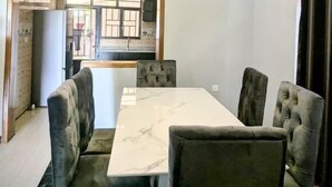 A dining room with a marble table and upholstered chairs, a chandelier, and a view of a kitchen through an open doorway. - Silver Budget & Travel Accommodation (Kigali)