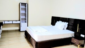 A neatly made bed with a black headboard, a bedside table with a drawer, and a white wardrobe with open doors. - Silver Budget & Travel Accommodation (Kigali)