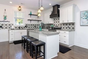Une cuisine moderne avec des meubles blancs, un îlot central doté de tabourets, une hotte noire et un pare-feu décoré d’un motif en étoile.