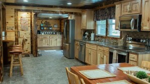 Une cuisine rustique avec des meubles en bois, un réfrigérateur en acier inoxydable et un coin repas comprenant une table et des chaises en bois.