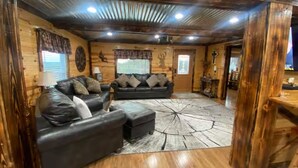 L’intérieur chaleureux d’un chalet, avec un revêtement mural en bois, deux canapés, un tapis et un plafond orné de poutres en bois.