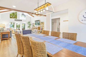 Ein Essbereich mit einem langen Holztisch, Korbstühlen und blauen Teppichen.