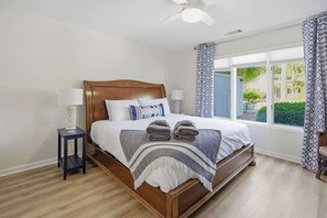A bedroom with a wooden bed, two bedside tables, a ceiling fan, and a window with patterned curtains.