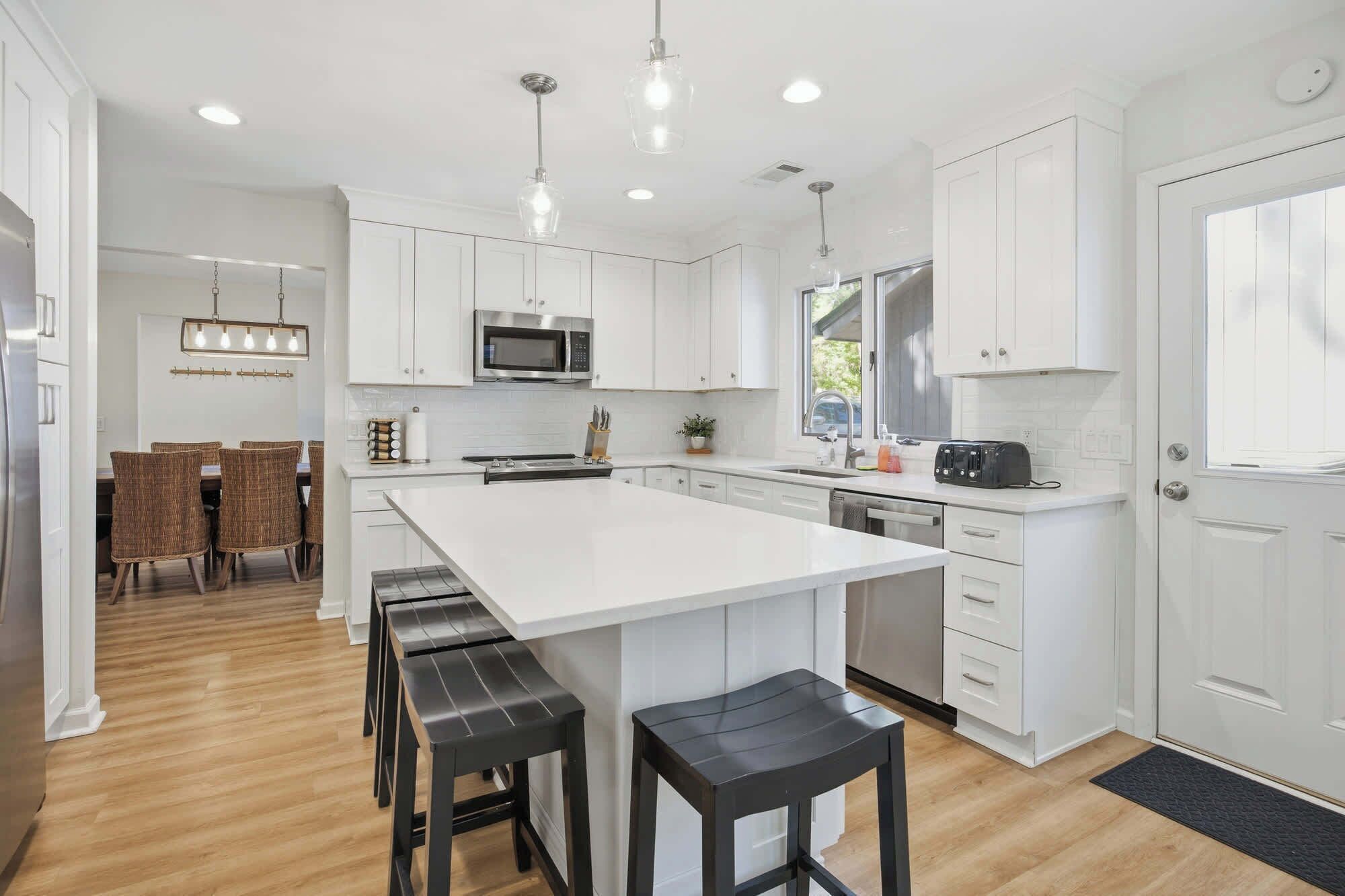 A modern kitchen with white cabinetry, a large island with bar stools, a microwave, and a toaster.