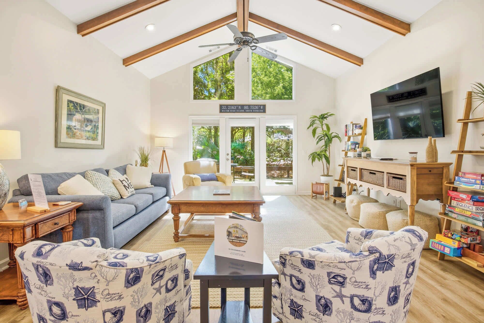 Amplia sala de estar con techo alto, ventilador de techo, televisor grande y vistas al exterior a través de puertas de cristal.