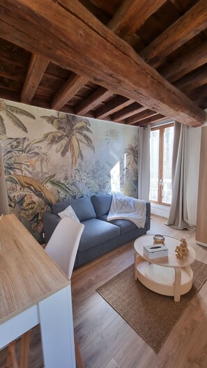 Ein Wohnzimmer mit Holzboden, einer Couch, einem Couchtisch und einer Wandmalerei von tropischen Pflanzen.