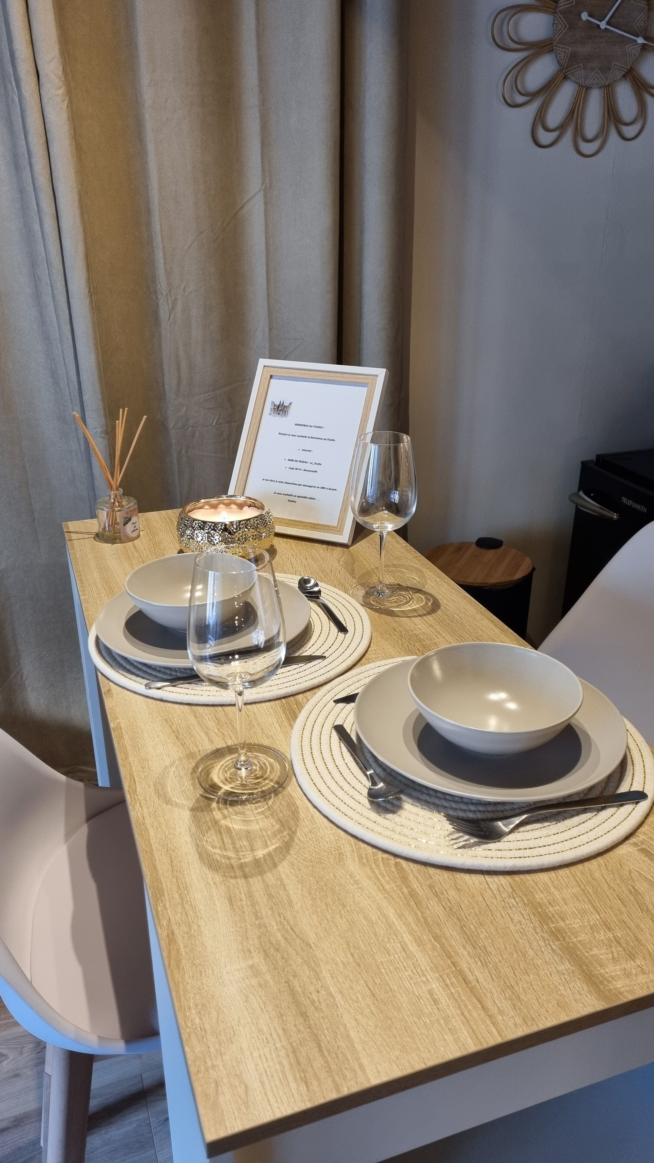 A dining table set with plates, glasses, and a candle, with a menu and a decorative item on the wall.