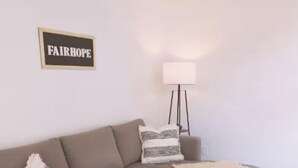 A living room with a brown sectional sofa, a wooden coffee table, a lamp, and a sign that reads "FAIRHOPE".