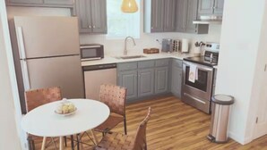 A compact kitchen with grey cabinets, a white refrigerator, a microwave, an oven, and a dining area with a round table and two chairs.