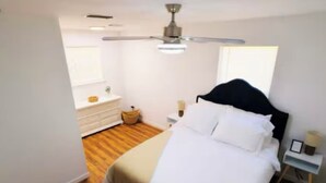 A bedroom with a bed, a nightstand, a bedside table, a ceiling fan, and a window.