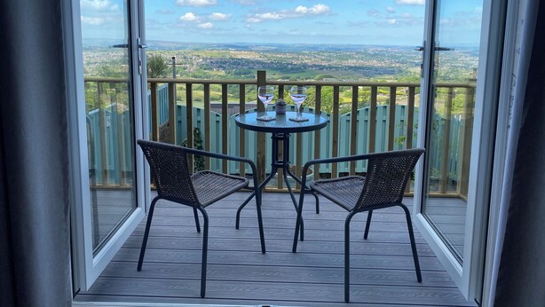 A balcony with a table and chairs, offering a view of a green landscape.